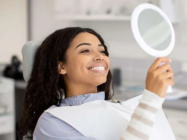 Mujer sonriendo frente al espejo después de un tratamiento de carillas y blanqueamiento dental.