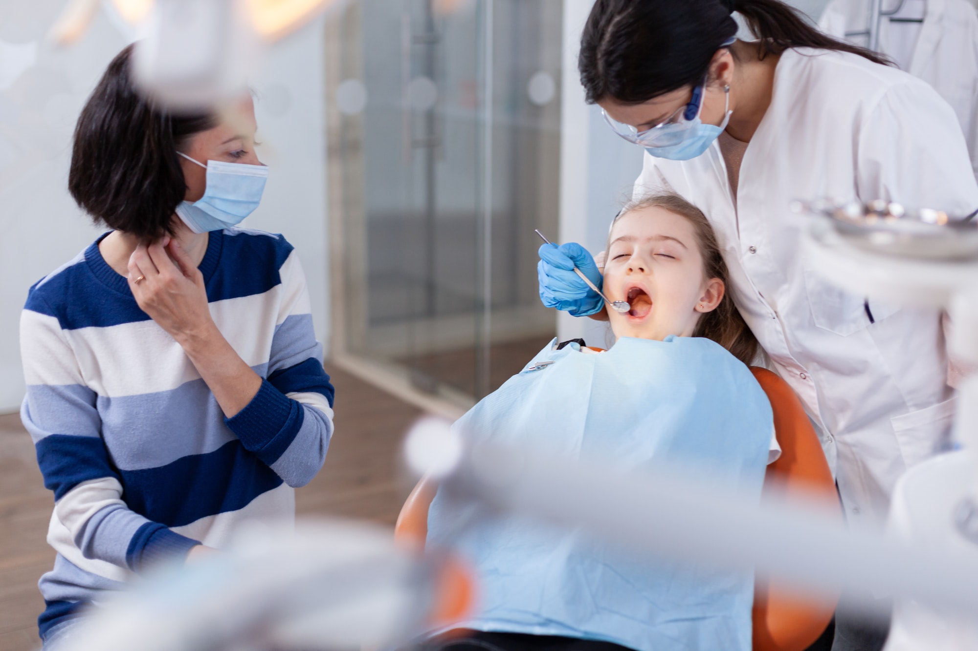 Un dentista examina a una niña con su madre durante una emergencia dental pediátrica.