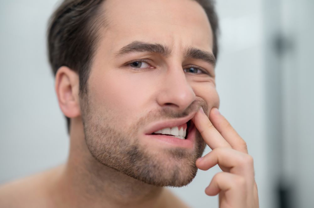 Hombre revisando encías inflamadas en el espejo, mostrando signos tempranos de enfermedad de las encías debido a una mala higiene dental.